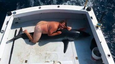 Homem gera polêmica ao posar nu e "montado" em tubarão morto