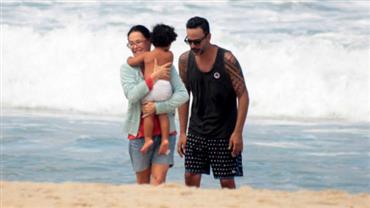 Em rara aparição, Carolina Ferraz vai à praia com filha e marido